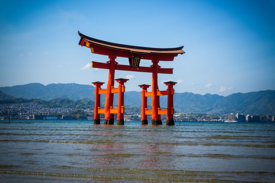 Red torii gate of Itsukushima Shrine standing in water at high tide with the island behind