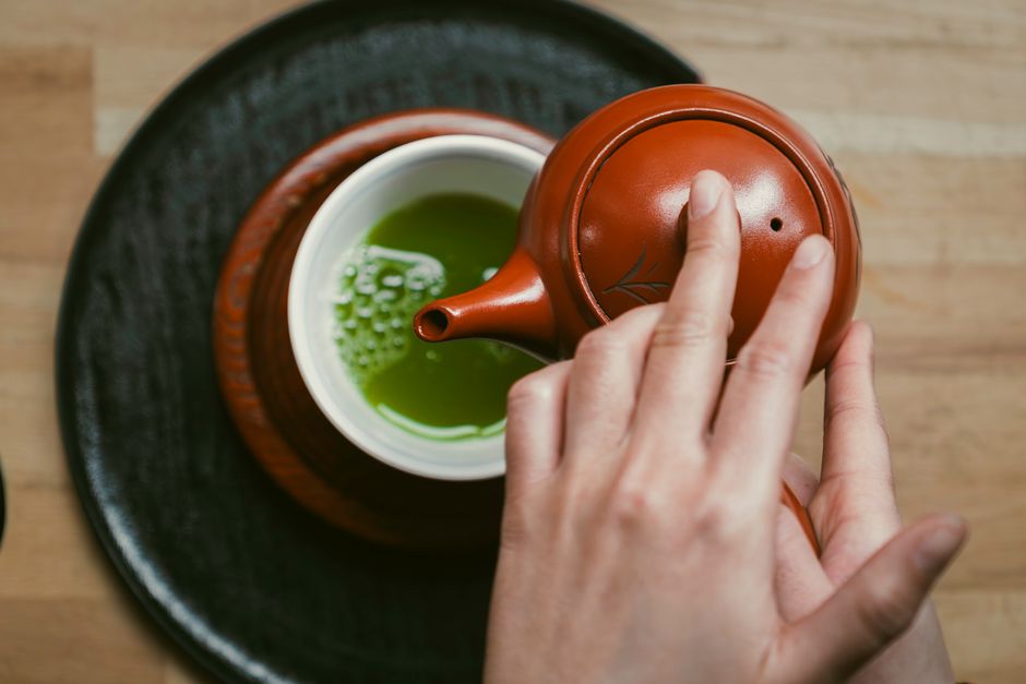 Hands turning a granite stone mill over bright green matcha powder in a tea house